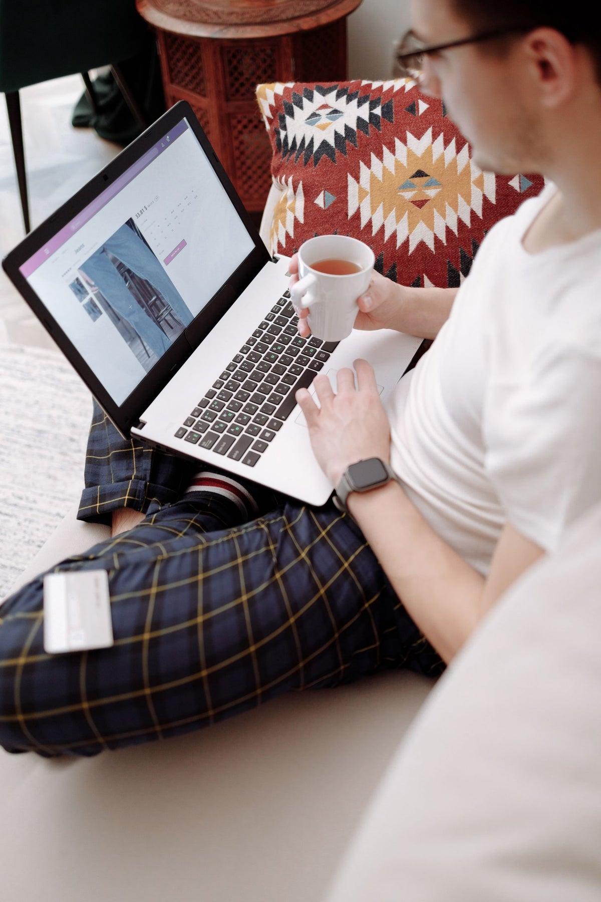 Man shopping for clothes online on a laptop with a cup of tea